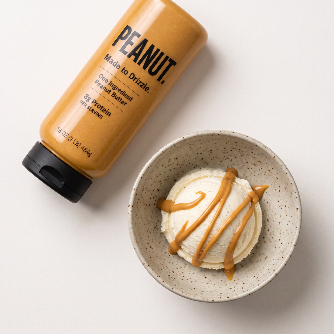 A scoop of vanilla ice cream drizzled with peanut butter, the bottle beside the bowl