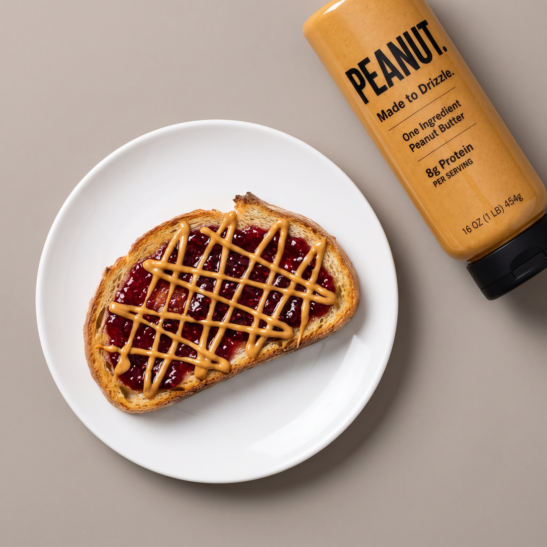 Toast with jam under a lattice of peanut butter, the bottle beside the plate