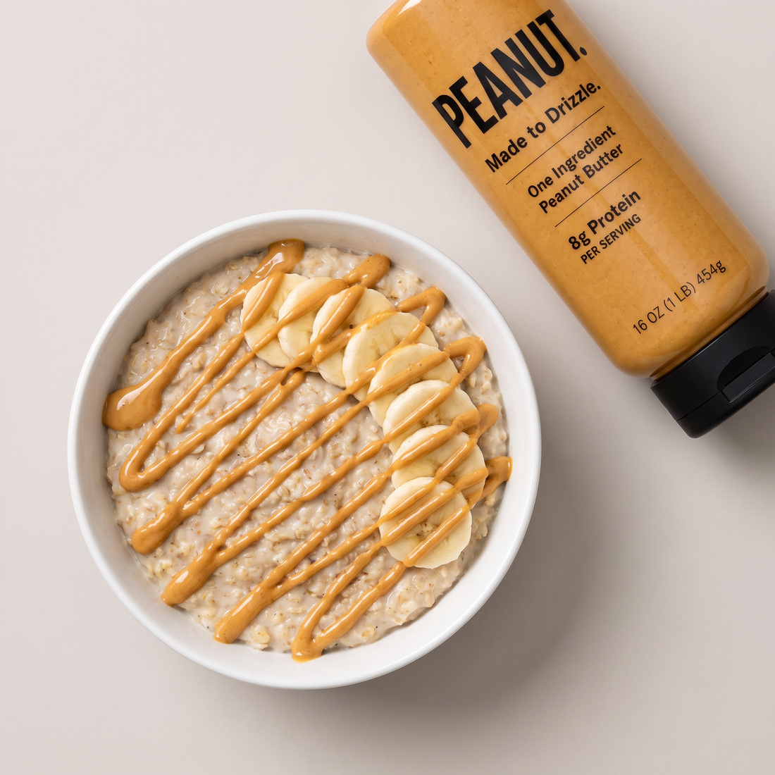 Oatmeal with sliced banana and a peanut butter drizzle, the bottle beside the bowl
