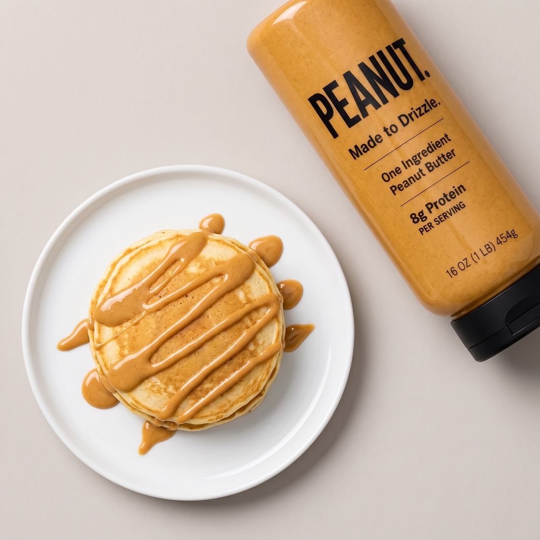 A stack of pancakes drizzled with peanut butter, the bottle beside the plate